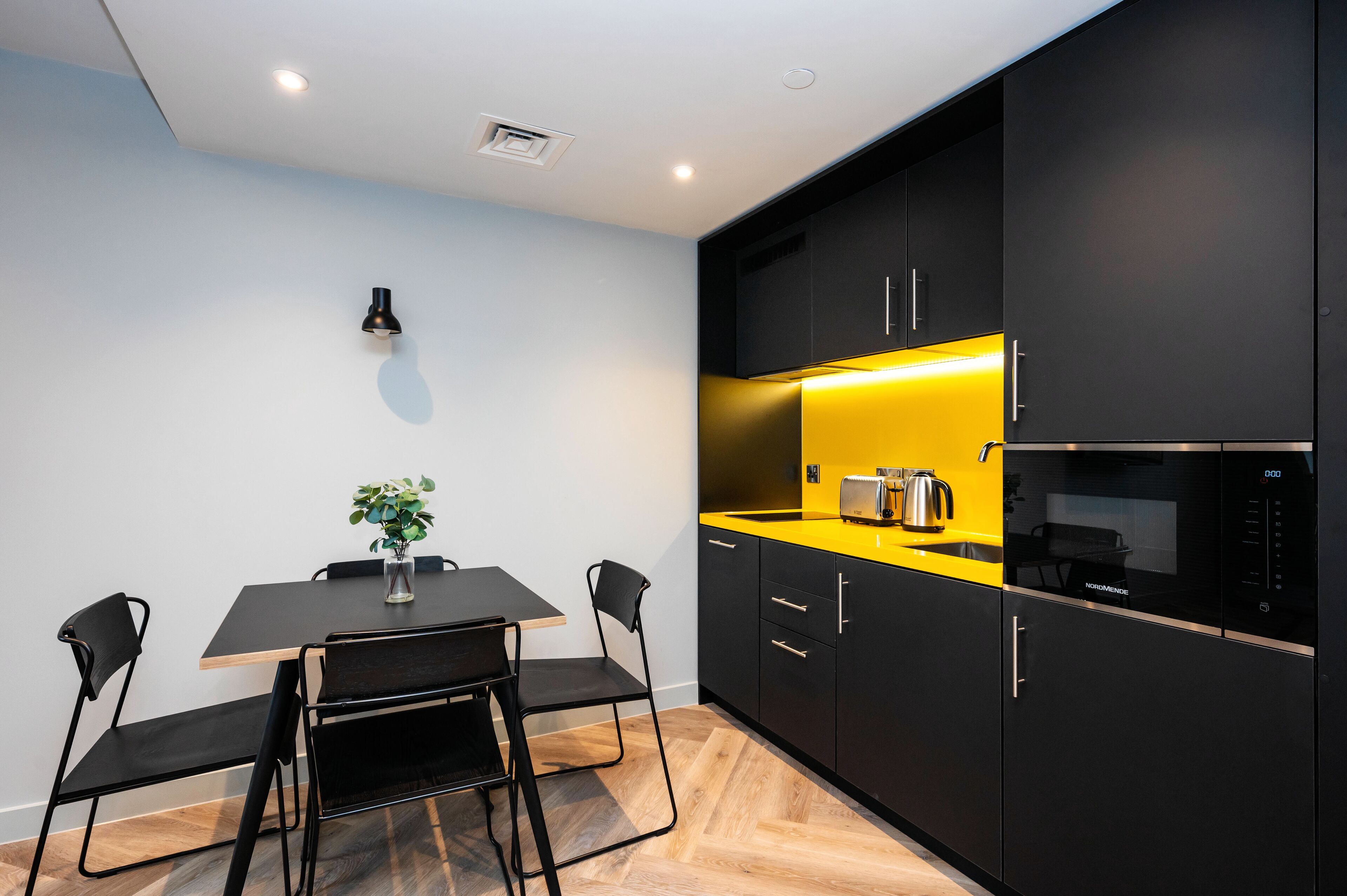 Una cocina moderna con armarios negros, encimera amarilla y microondas integrado.