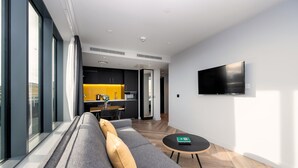 Una sala de estar moderna con un sofá gris, una mesita redonda y un televisor de pantalla plana montado en la pared.