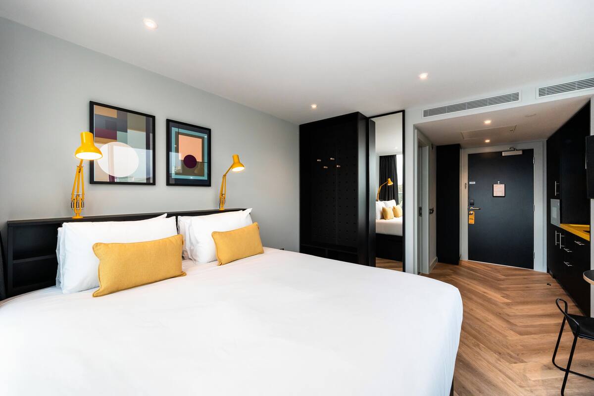 A modern hotel room with a large bed, two bedside lamps, and artwork on the wall.