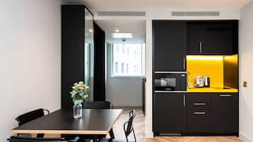A modern kitchen with black cabinets and a yellow countertop, a dining area with a wooden table and black chairs, and a view of the city through a window.