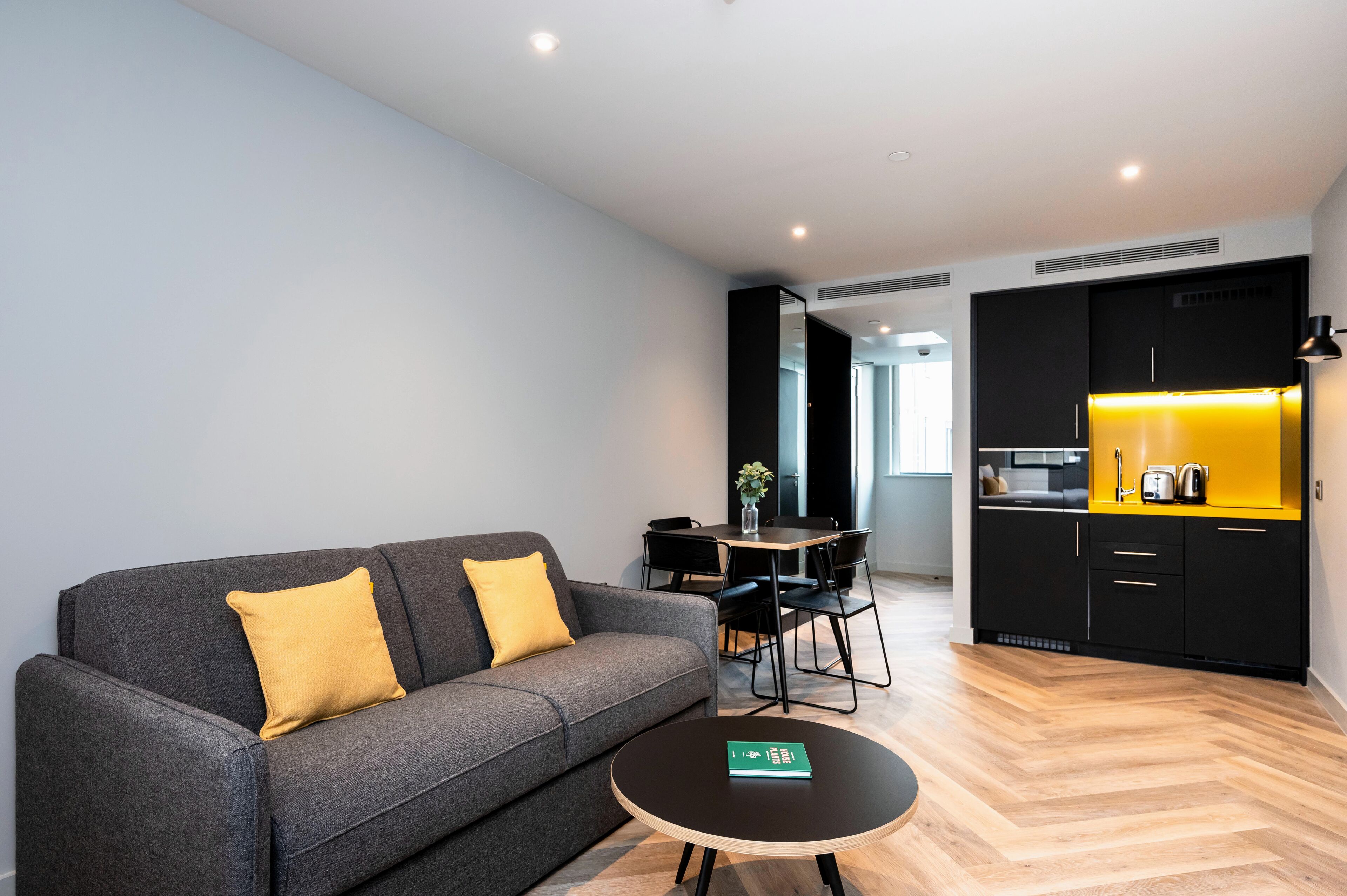 A modern living room with a grey sofa, yellow cushions, a round coffee table, and a dining area with a black table and chairs.