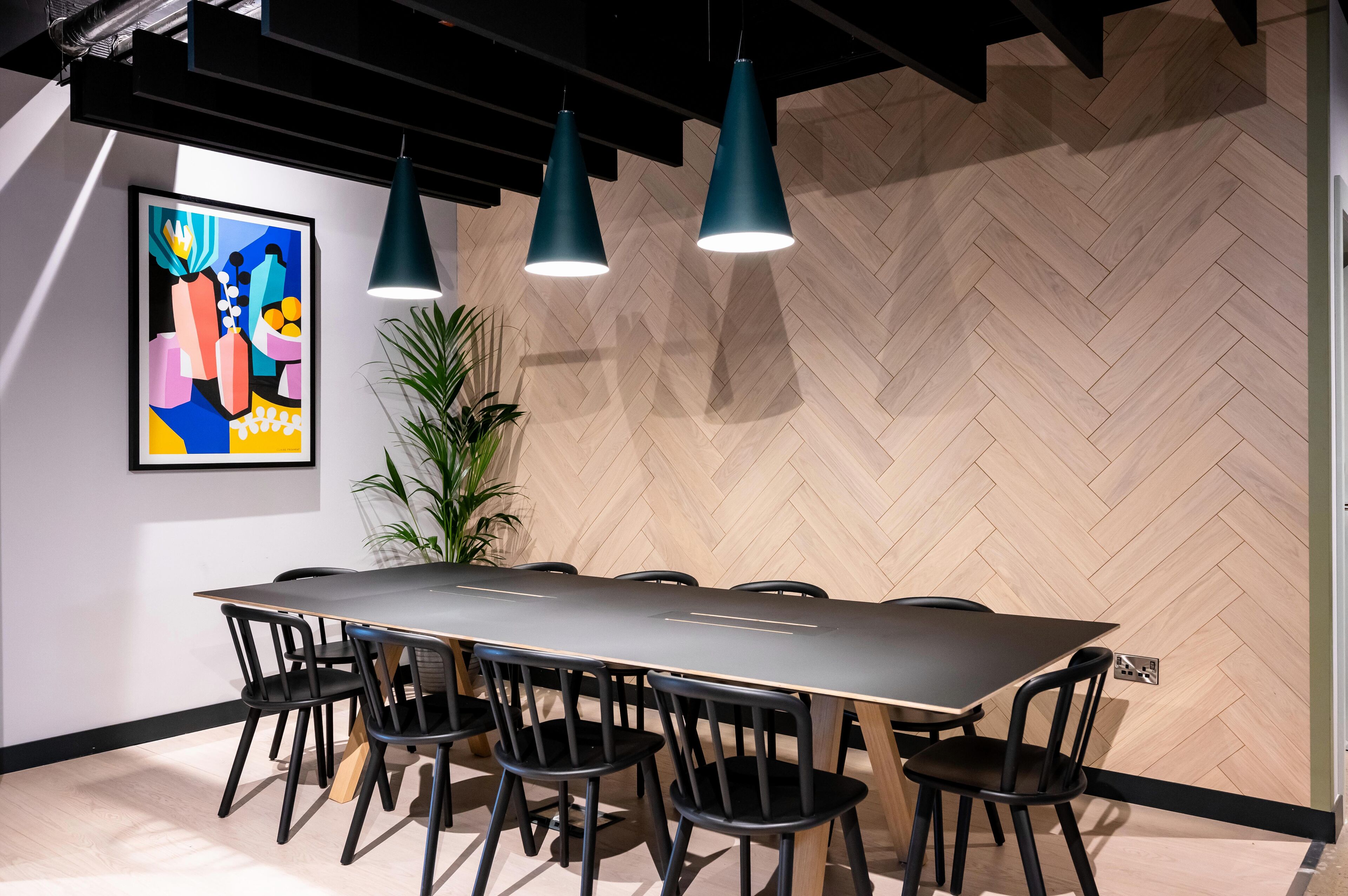 A conference room with a long table, black chairs, and teal pendant lights.