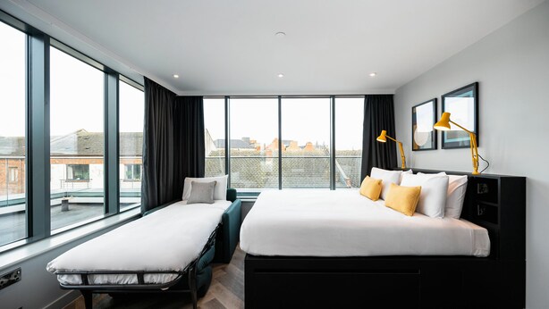 Una habitación de hotel moderna con dos camas, ventanas amplias y vistas a la ciudad.