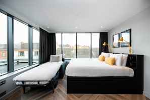 A modern hotel room with two beds, large windows, and a city view.