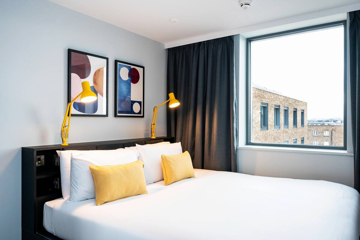 A hotel room with a large bed, two bedside lamps, a nightstand, and artwork on the wall.