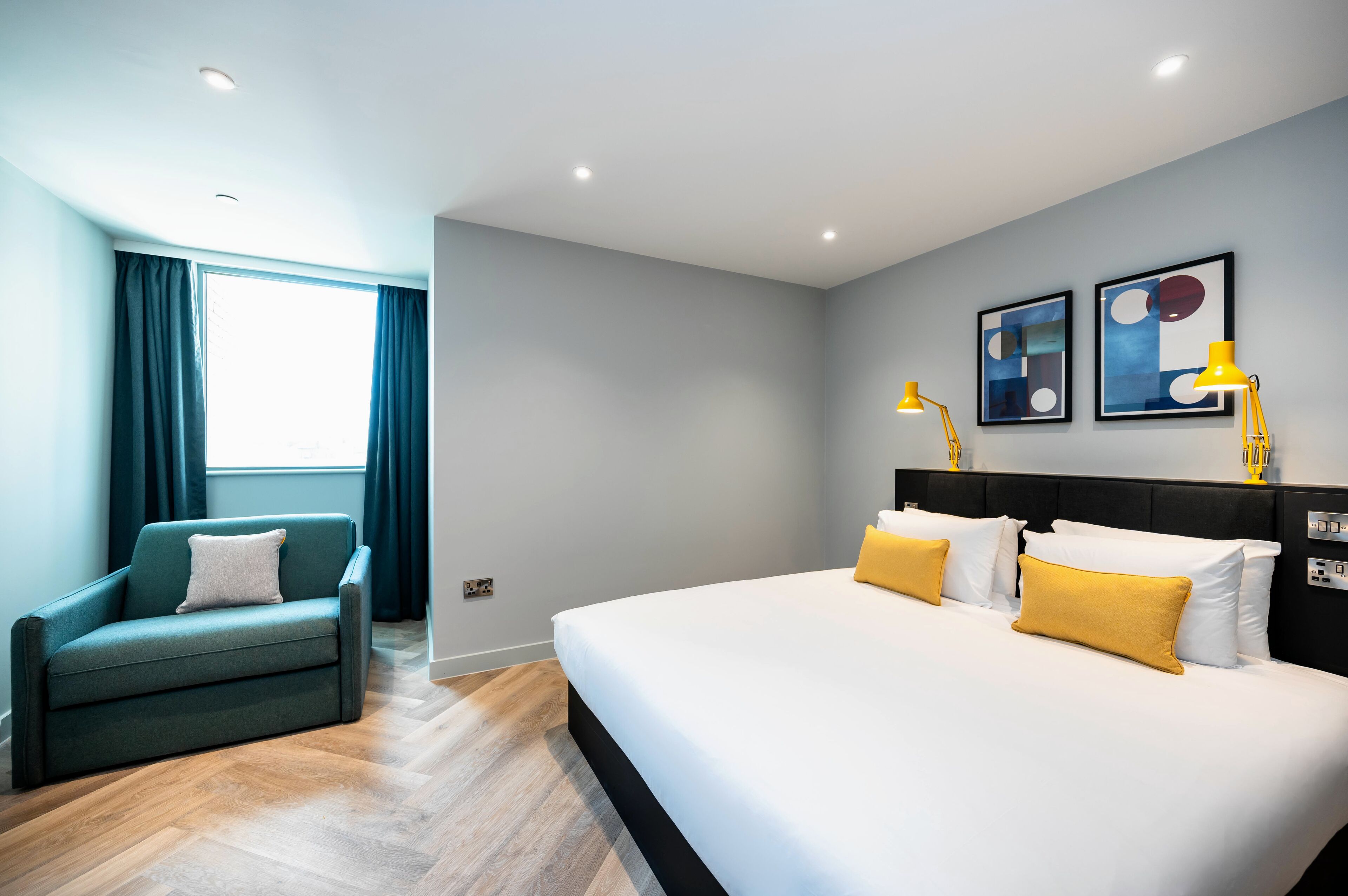 A modern hotel room with a large bed, a sofa, and artwork on the wall.