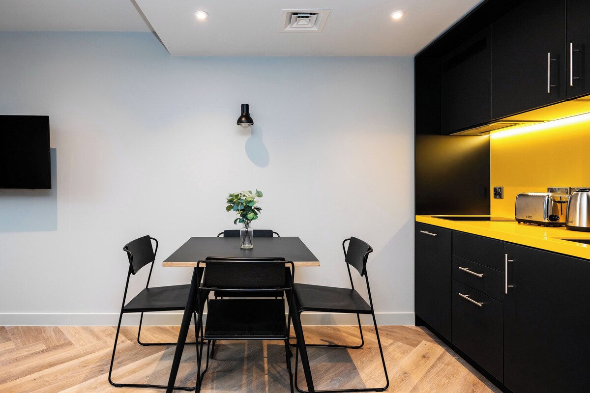 Una cocina moderna con armarios negros, encimera amarilla y una mesa de comedor negra con sillas.