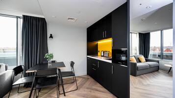 A modern apartment with a dining area, kitchenette, and a sofa by a large window.