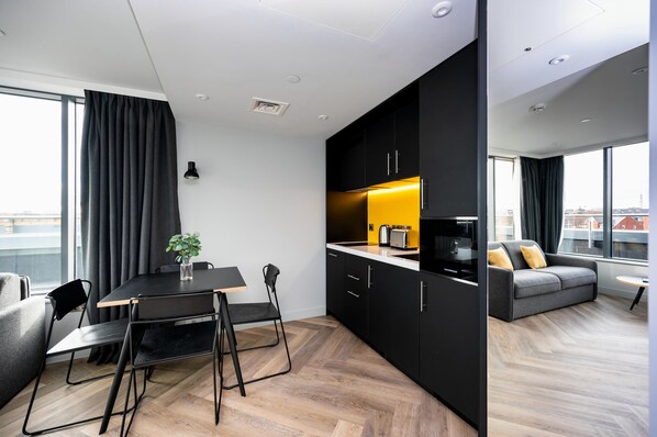 A modern apartment with a dining area, kitchenette, and a sofa by a large window.