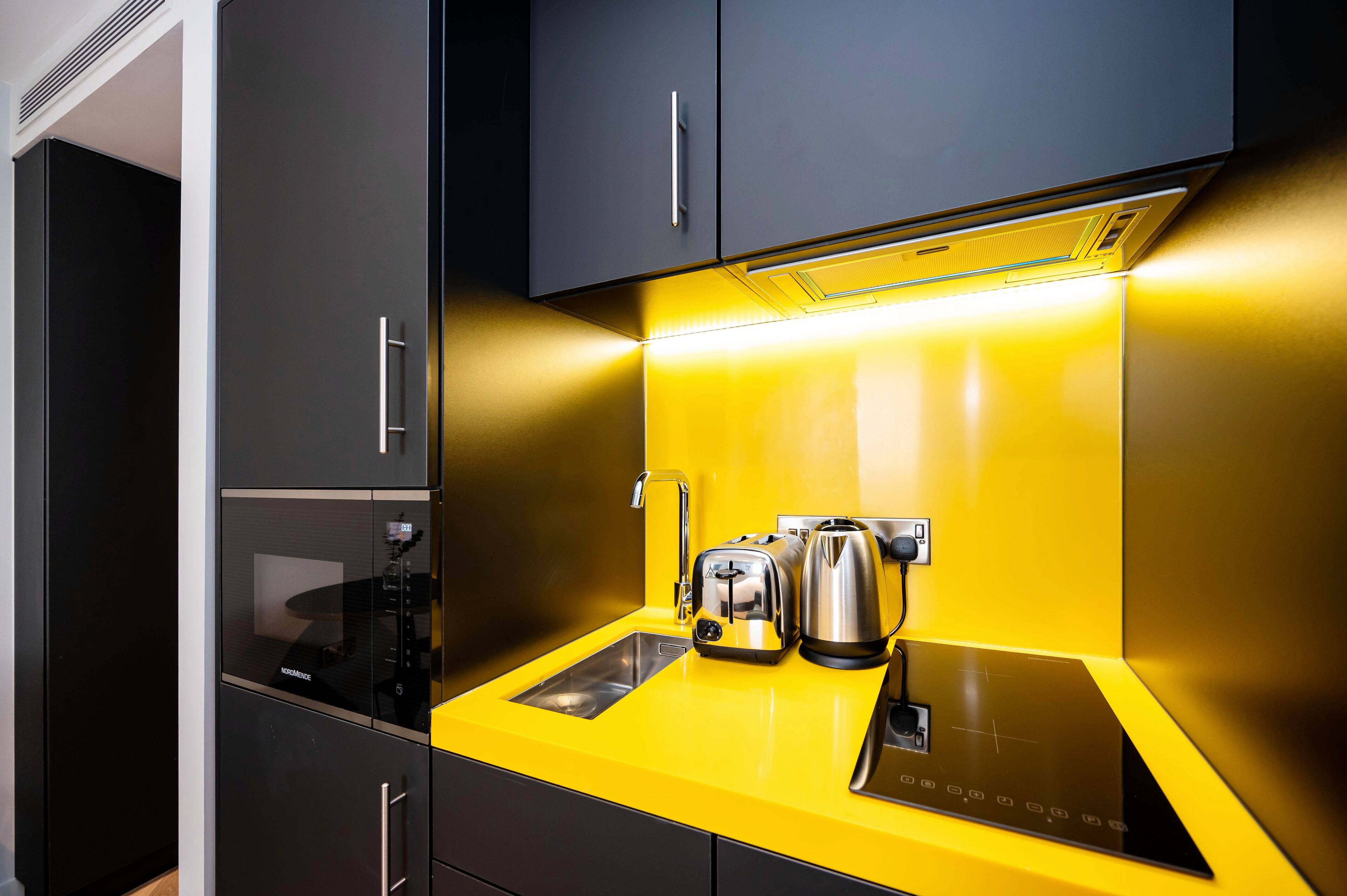 Una cocina moderna con un refrigerador negro, horno empotrado y encimera amarilla con una tetera y un tostador.