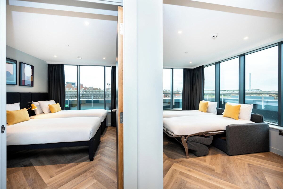 Habitación de hotel moderna con una cama grande, un sofá cama y vistas a un puente.