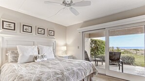 Ein Schlafzimmer mit einem großen Bett, einem Deckenventilator und Blick ins Freie durch eine Schiebetür.