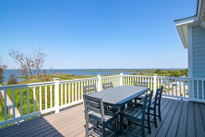 A wooden deck with a table and chairs, white railings, and a view of a body of water and distant land. - Pier, Pool, Sunsets • Luxe Soundfront Retreat (Corolla)