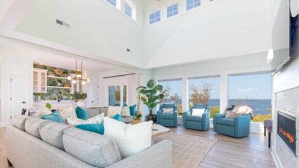 A spacious living room with a large gray sofa, blue armchairs, and a fireplace. - Pier, Pool, Sunsets • Luxe Soundfront Retreat (Corolla)
