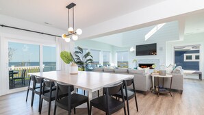 A modern living room with a large dining table, a fireplace, and a view of the sea. - Pier, Pool, Sunsets • Luxe Soundfront Retreat (Corolla)