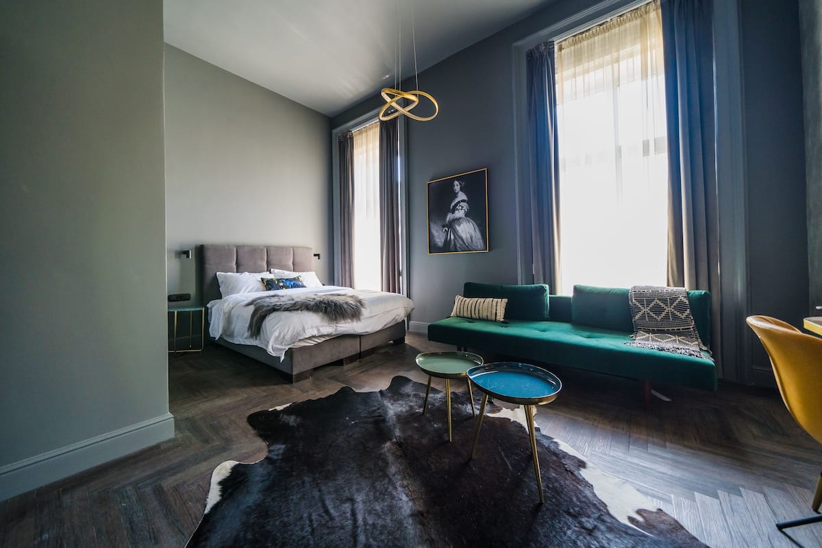 A modern bedroom with a bed, a green sofa, a yellow chair, and a large rug.