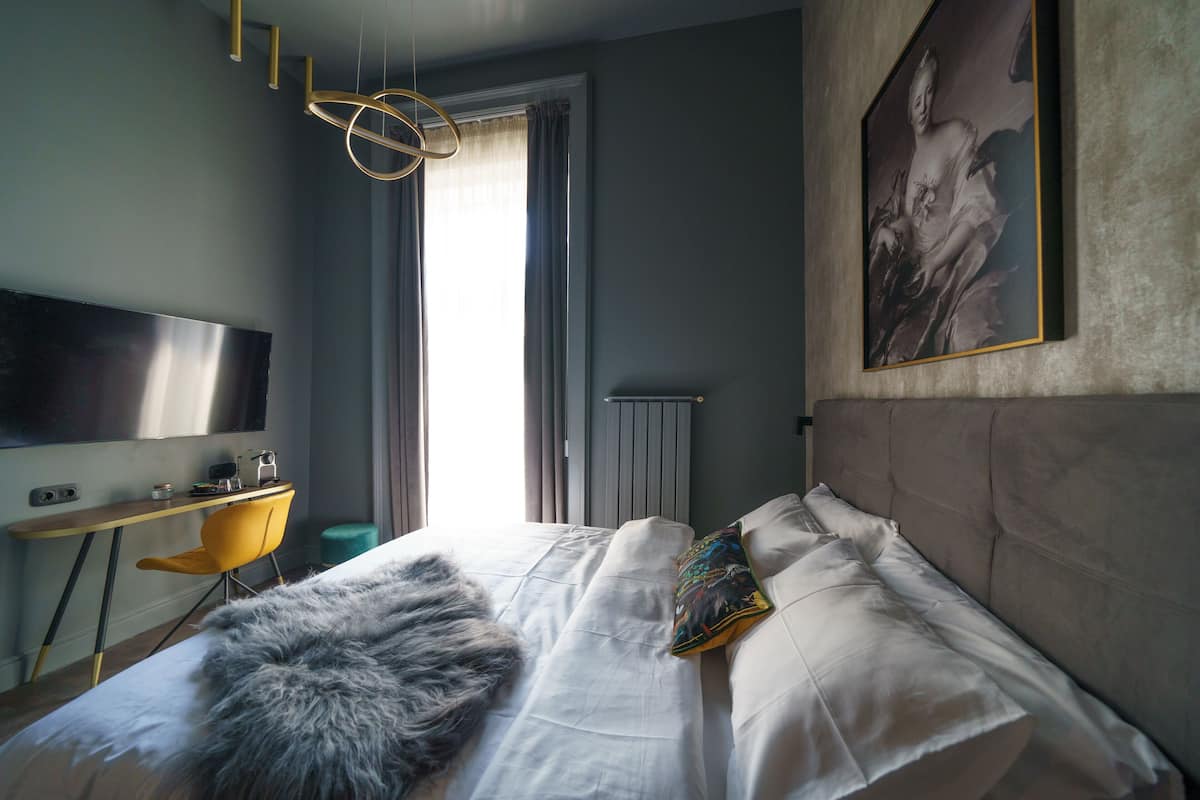 A modern bedroom with a bed, a desk, a chair, a television, and a painting on the wall.