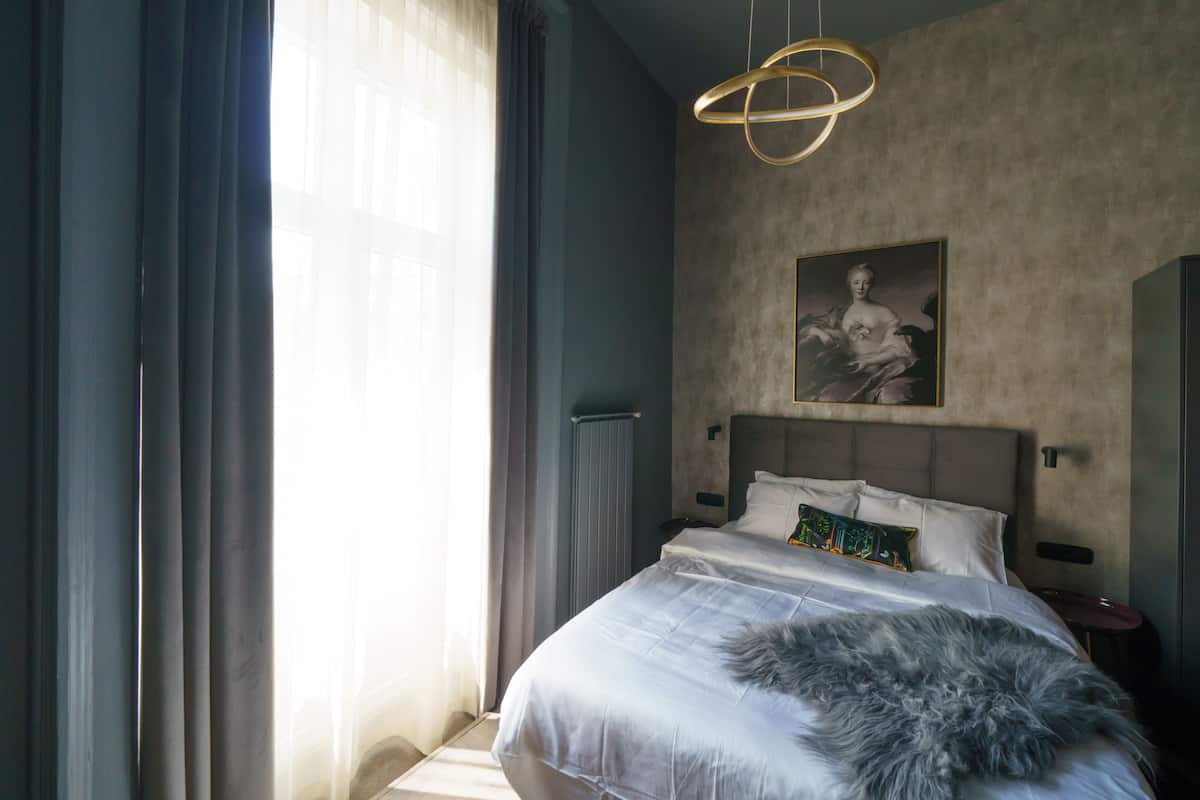 A modern bedroom with a large bed, a fluffy throw, a unique light fixture, and a painting on the wall.