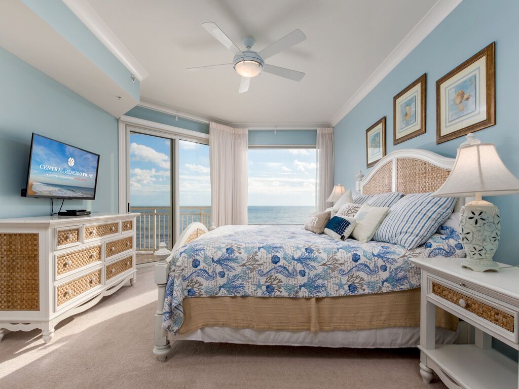 Ein Schlafzimmer mit Bett, Fernseher, Deckenventilator, Kommode und Blick auf den Ozean.