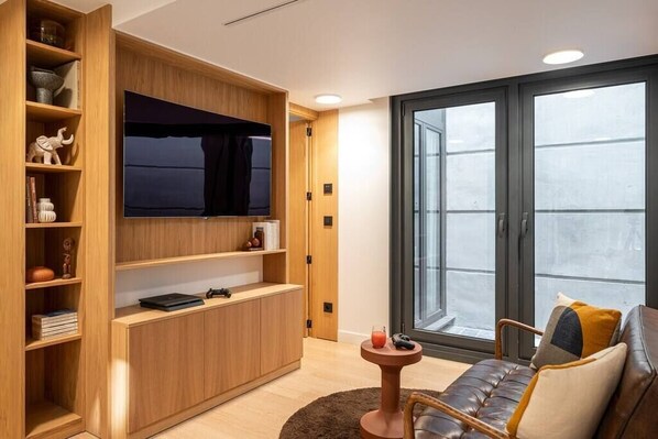 Un salon moderne avec un meuble de rangement en bois pour l’équipement audiovisuel, un canapé en cuir et une grande fenêtre offrant une belle vue.