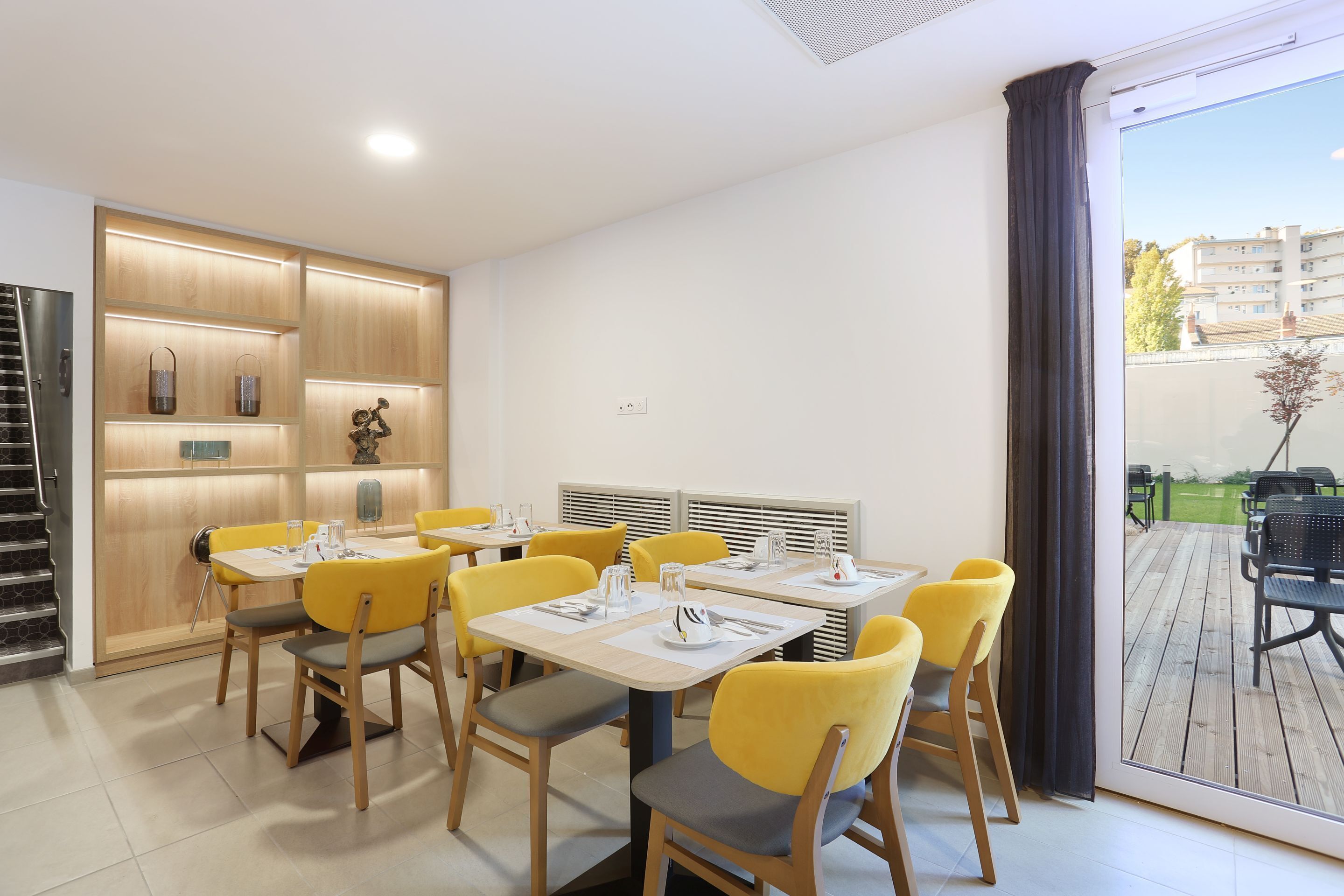 A dining area with wooden cabinets, yellow chairs, and tables set for four.