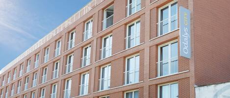 Un immeuble à plusieurs étages, doté d’une façade en briques, de nombreux balcons et d’une enseigne indiquant qu’il s’agit d’un hôtel.
