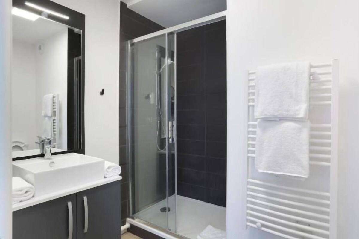 A modern bathroom with a glass-enclosed shower, a white sink, and a towel rack.
