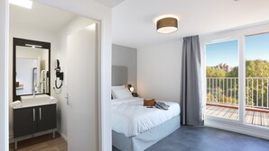 Una habitación de hotel moderna con una cama grande, un baño con lavamanos y espejo, y un balcón con vistas.