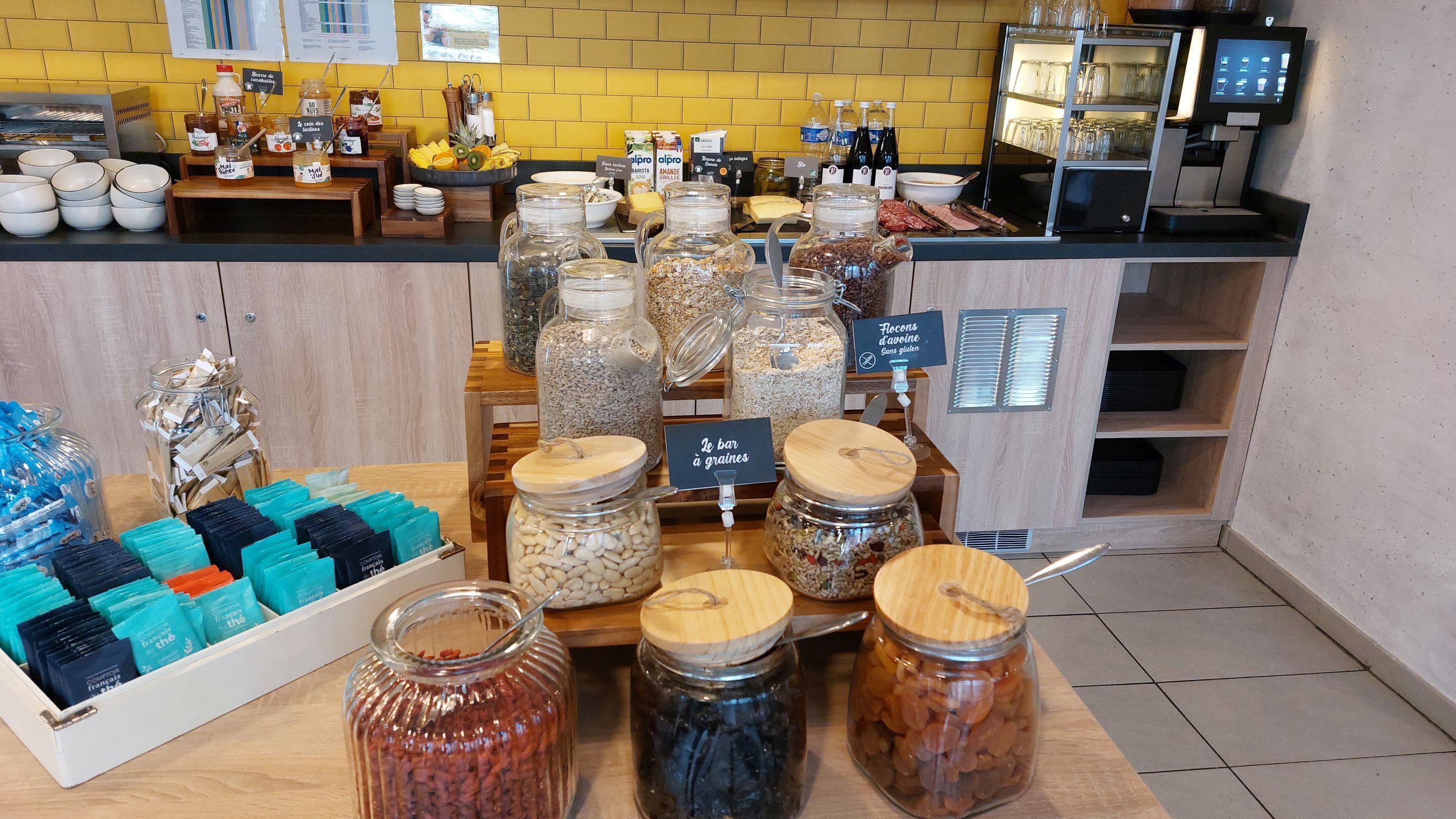 A food display with various jars of grains and spreads, a coffee machine, and a menu board.