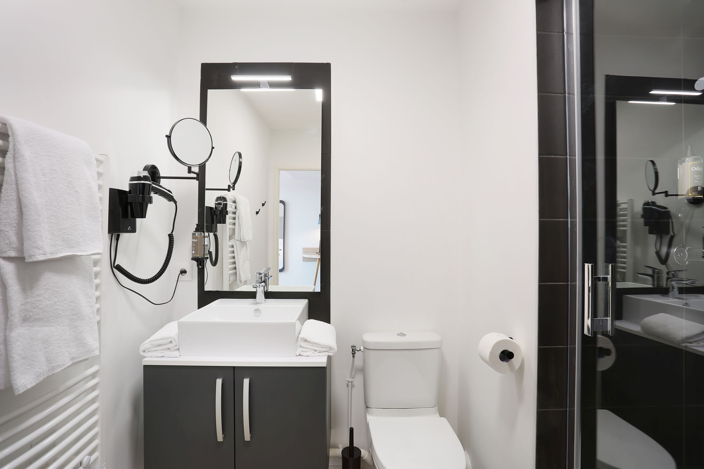 A modern bathroom with a white sink, dark cabinet, and a glass shower enclosure.