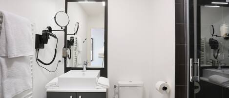 A modern bathroom with a white sink, dark cabinet, and a glass shower enclosure.