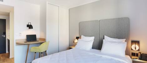 Une chambre d’hôtel moderne, dotée d’un grand lit, d’un bureau avec un ordinateur portable, d’une chaise et d’une table de chevet avec une lampe et un téléphone.