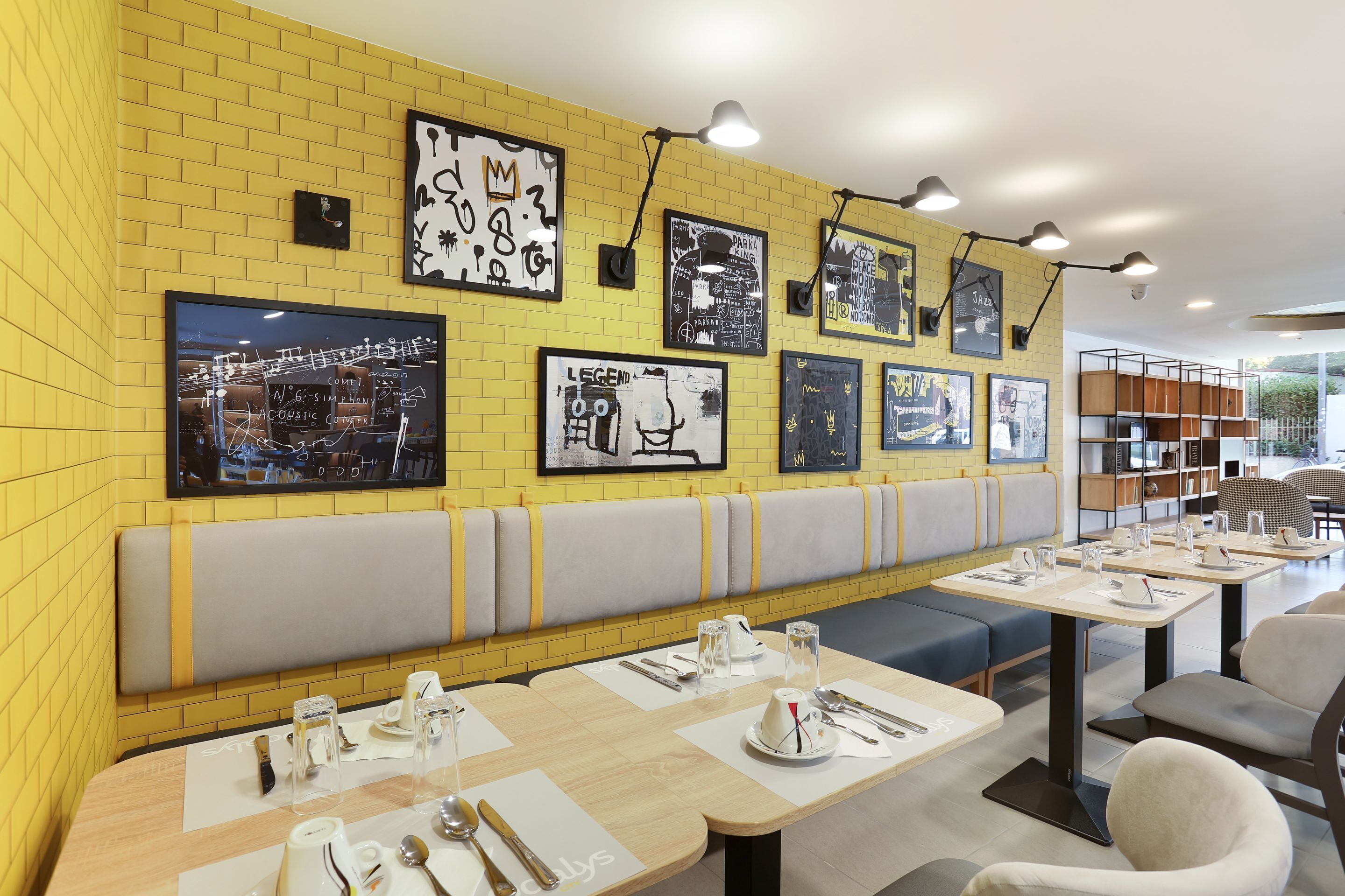 Un restaurant aux murs en briques jaunes, orné de nombreux tableaux encadrés, et doté d’un long banc servant de banquette.