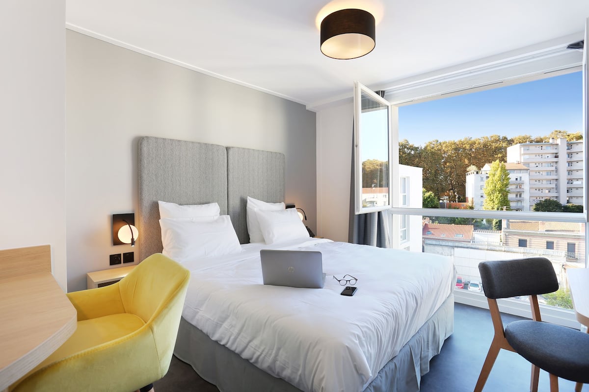 A modern hotel room with a large bed, a laptop, and a pair of glasses on the bed.