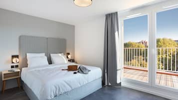 A modern hotel room with a large bed, two bedside tables with lamps, a view of the outdoors through a balcony.