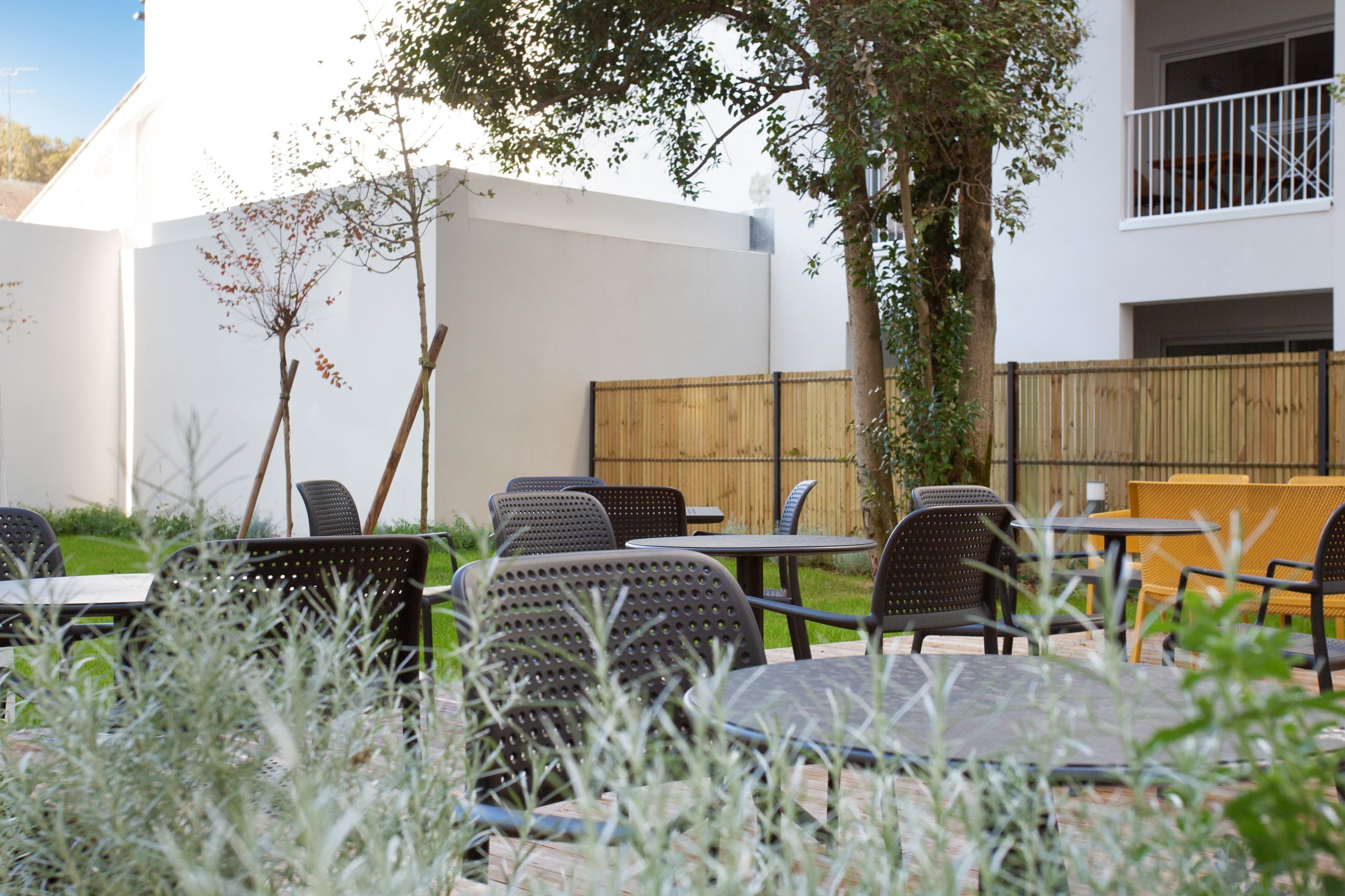 Un espacio al aire libre con mesas y sillas, rodeado por una valla de madera y un edificio blanco.