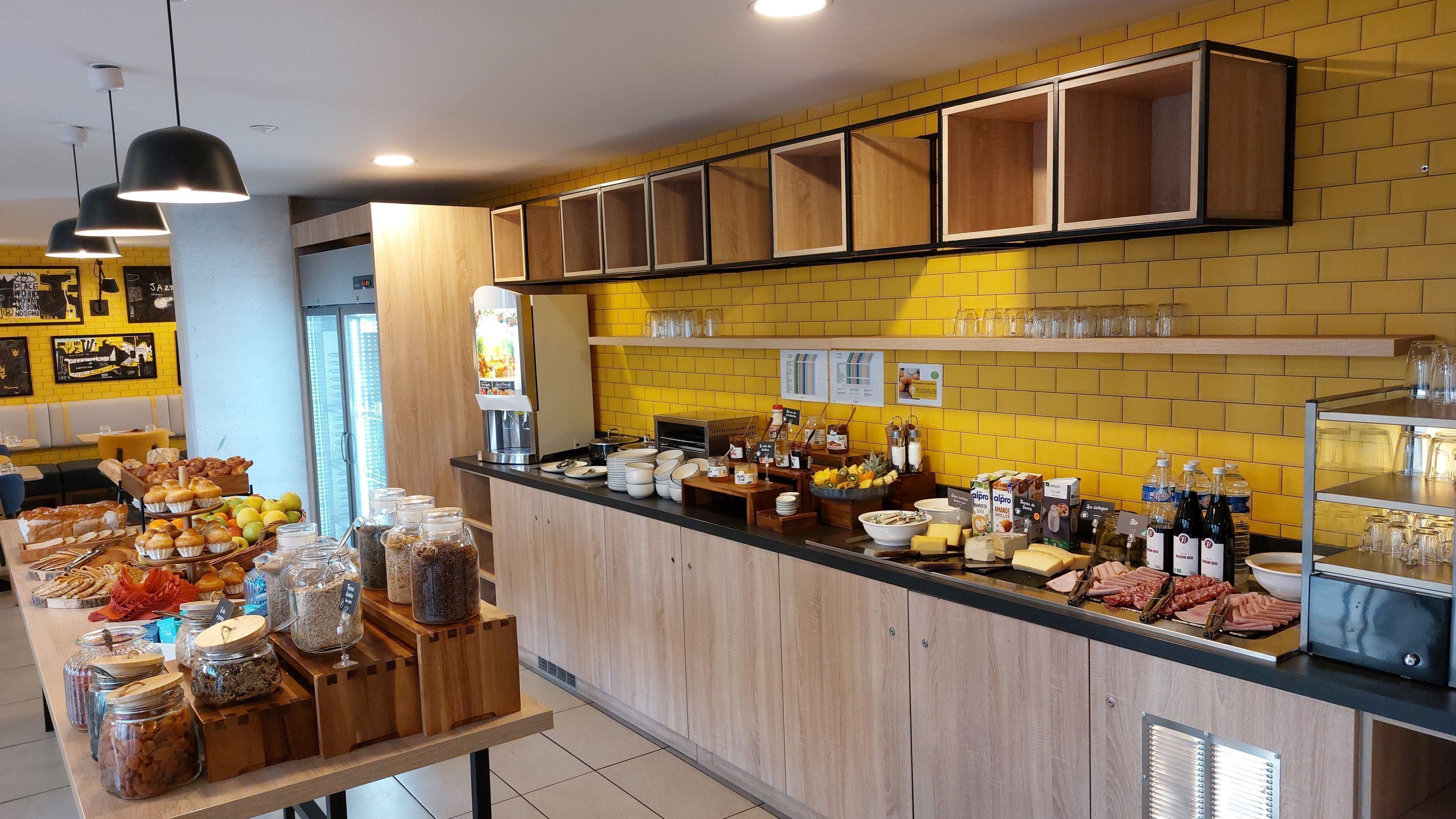 Un buffet de petit-déjeuner proposant une variété d’aliments et de boissons, des meubles en bois et un mur recouvert de carreaux jaunes.