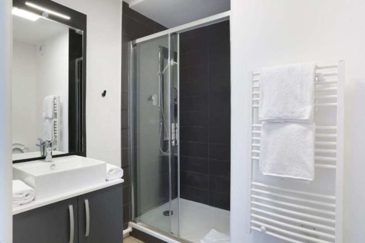 A modern bathroom with a glass-enclosed shower, a white sink, and a towel rack.