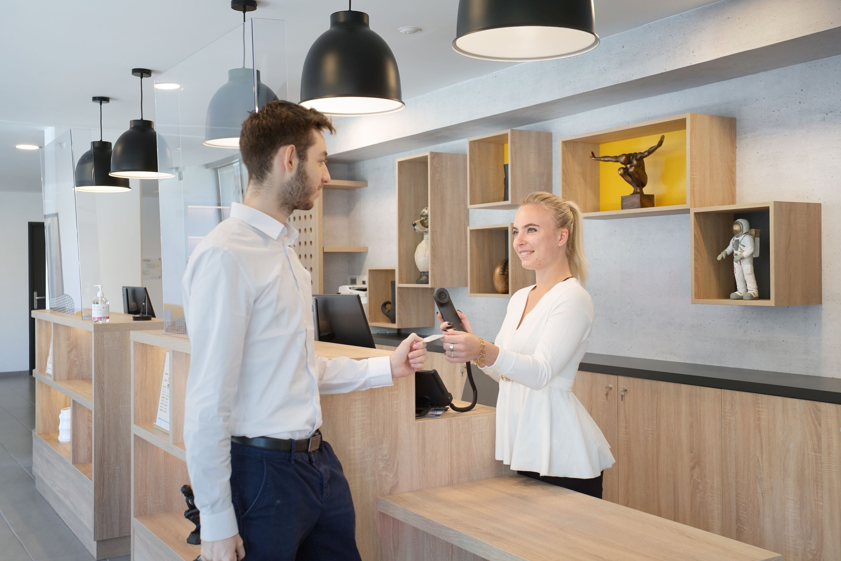A reception area with a wooden reception desk, black pendant lights, and shelves with decorative items.