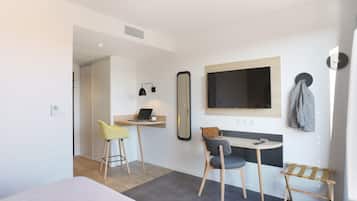 Ein modernes Hotelzimmer mit einem Bett, einem Schreibtisch mit einem Laptop, einem Spiegel und einem Fernseher.
