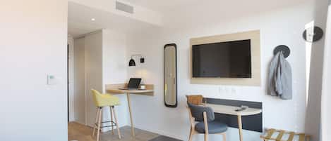 Ett modernt hotellrum med en säng, ett skrivbord med en bärbar dator, en spegel och en tv.