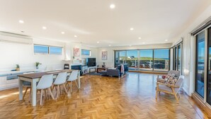 Een ruime woonkamer met een houten visgraatvloer, een eettafel met stoelen, een bank en een televisie.