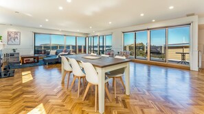 Un salón amplio con suelo de parqué en espiga, una gran mesa de comedor con sillas, un sofá y vistas a través de amplias ventanas.