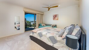 Un dormitorio con una cama, ventilador de techo, ventana con cortinas, una puerta y una obra de arte colgada en la pared.