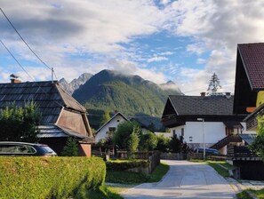 Traditional houses line a serene street, surrounded by well-maintained hedges and a pathway leading to the mountains.