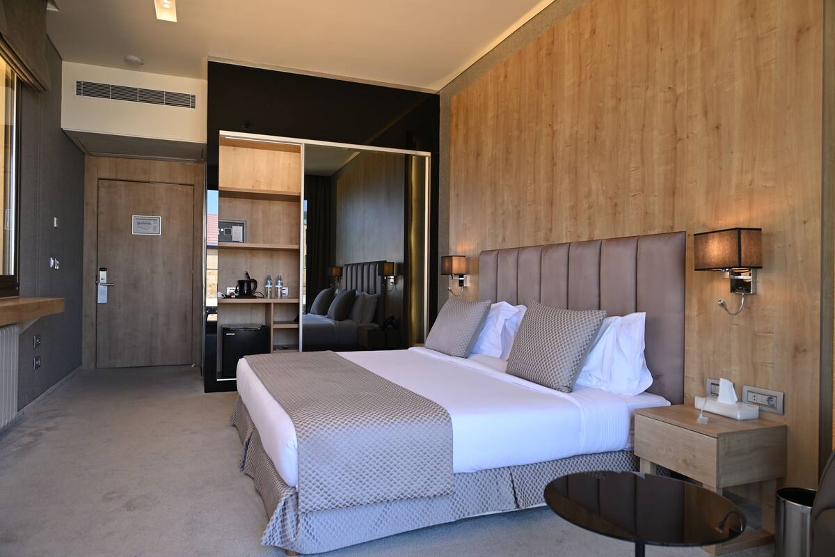 A hotel room with a large bed, bedside tables, a desk, and a wardrobe.