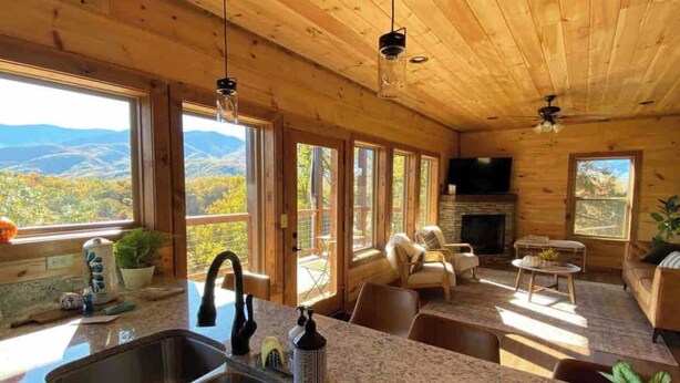 Ein gemütliches Blockhaus mit Küche, Essbereich und Kamin. Große Fenster bieten Blick auf die Berge.