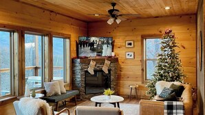 Ein gemütliches Blockhaus mit Holzwänden, einem Steinkamin, einem Weihnachtsbaum und einer Sitzecke mit Sofa und Sesseln.