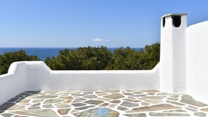 A stone-tiled patio with a white wall and a view of the sea. - Santa Flora 3 bedroom House (Paros)