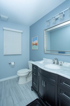 A bathroom with a white toilet, a sink with a marble countertop, and dark cabinets. - Villa Patricia Surrounded by Trees (Bloomfield Hills)